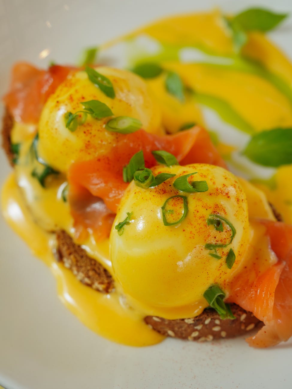Close-up of Eggs Benedict featuring poached eggs on a sesame seed toast with salmon, garnished with green onions and a creamy hollandaise sauce.
